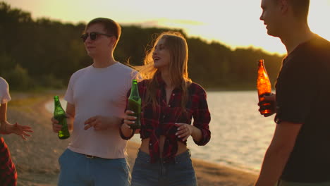 Young-teens-are-dancing-on-the-open-air-party-with-beer.-They-are-enjoying-the-summer-sunset-with-friends-on-the-beach-at-beautiful-red-sunset.